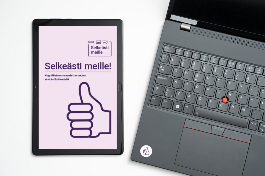 Pöydällä tietokone ja tabletti. Tabletin ruudulla on Selkeästi meille kognitiivisen saavutettavuuden arviointikriteeristö.