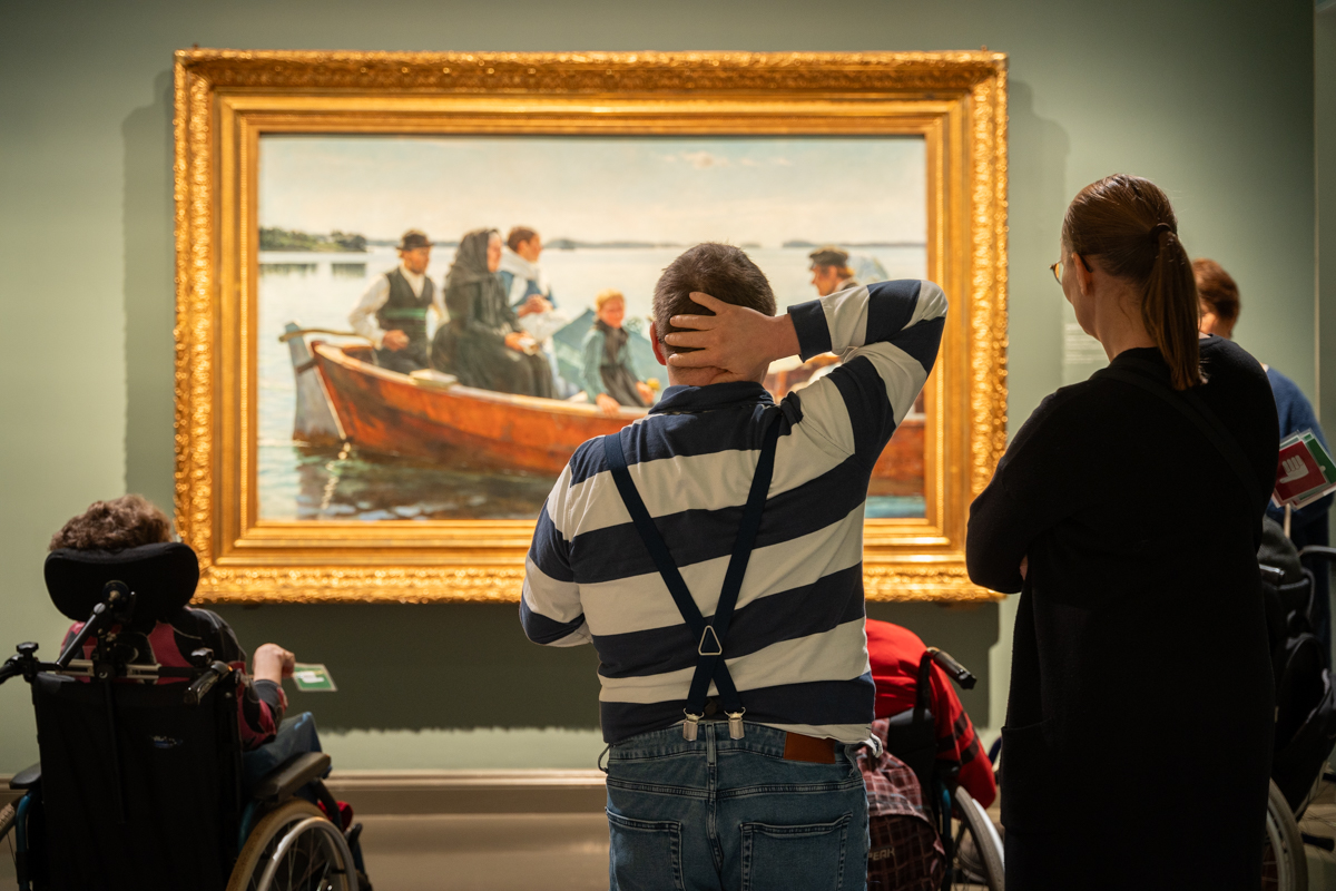Valokuva taidemuseosta, jossa ryhmä katsoo maalausta lapsen ruumissaattoveneestä.
