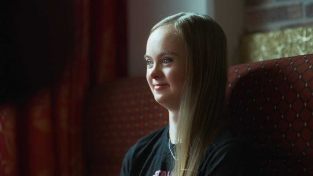 Nainen istuu ravintolassa, katsoo eteenpäin ja hymyilee.