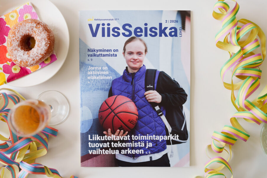 ViisSeiska-lehti pöydällä. Lehden kannessa nuori nainen pitää koripalloa. Ympärillä on serpentiiniä, munkkeja ja simaa.