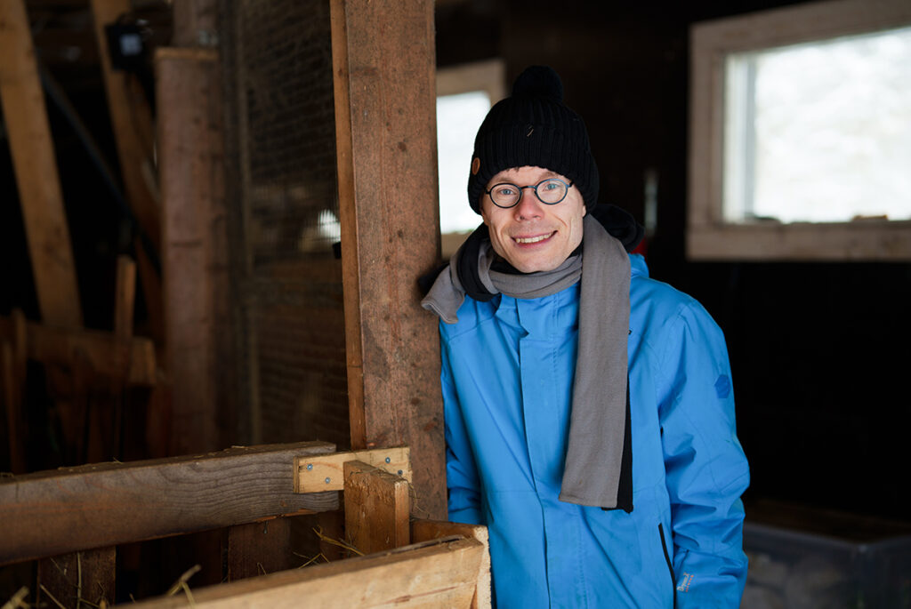 Mies nojaa lampolan tolppaan ja hymyilee kohti katsojaa.